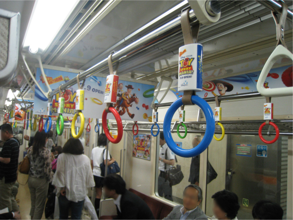 通常は三角形の吊り輪を期間限定で、赤・黄・青・緑のカラフルな輪っかにしている（東京メトロ銀座線）。